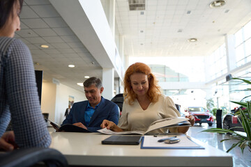 Pleasant couple looking through advertising leaflets in car dealership