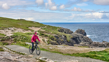nice senior woman on mountain bike, cycling on the cliffs of Malin Head, the northern most point of...