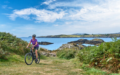 nice senior woman on mountain bike, cycling on the cliffs of Toormore,County Cork in southwestern Ireland