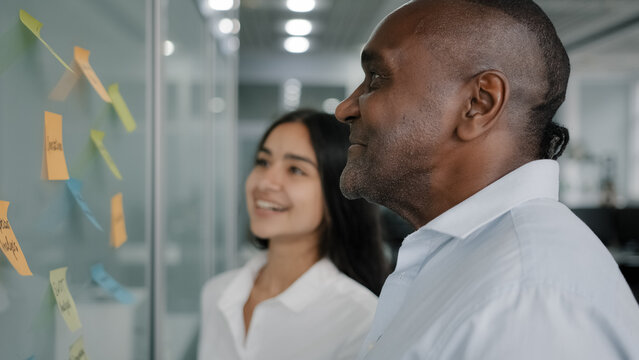 Corporate team business partners colleagues look at paper memo stickers on wall discuss project giving business advice managing tasks structure sticky notes brainstorming teamwork at office meeting - Powered by Adobe