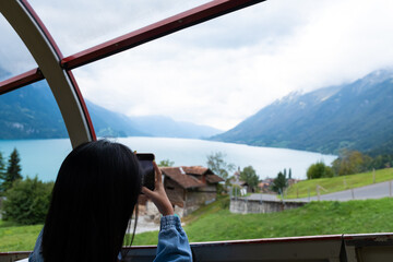 Young Asian tourist women using her smartphone to taking photo of natural scene while travel in Brienz Switzerland. Tourist attraction view point on the way to Rothorn Bahn with copy space.