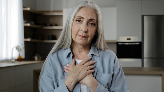 Caucasian Old Mature Woman Put Folded Palms On Heart Keeps Wrinkled Hands On Chest Make Thankful Trust Gesture Friendly Symbol Express Sincere Feelings Smile Look At Camera Believe And Charity Concept