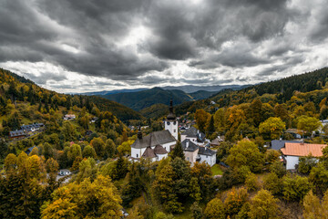 view of the village and Roman Catholic church in Spania Dolina with colorful autumn forest - obrazy, fototapety, plakaty