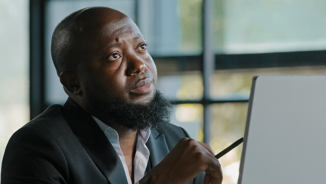 Doubtful thoughtful african american team leader male coach think question solve daily working task in mind has dilemma self brainstorming reflective turns pen by hand create project business strategy