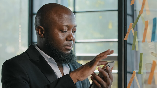 African american businessman stand near sticker board read news on smartphone make online order booking delivery at office use business mobile apps scrolling sensor display chatting in social networks