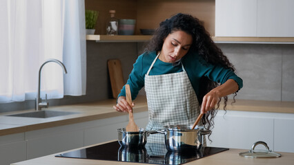 Busy arabian mom attractive curly housewife chef wears apron cooking breakfast at home kitchen...