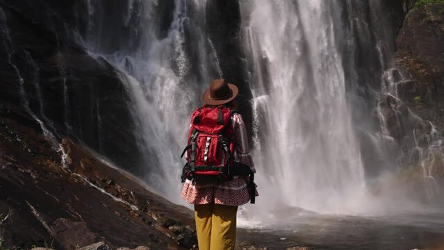 young girl standing with backpack observing a forest landscape with waterfall. woman in front of a waterfall enjoying the nature. Active turism norway