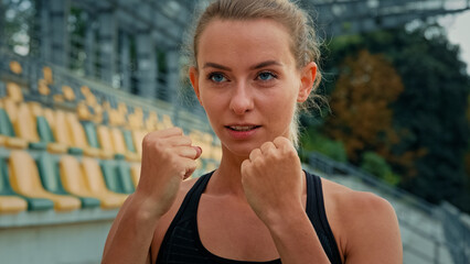 Motivated female fighter athlete with clenched fists standing in boxing stance punching air dynamic...