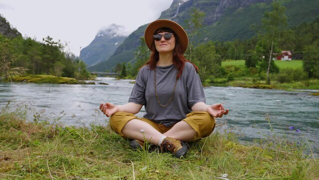 Travel woman in a hat and sunglasses doing meditation exercises against picturesque landscapes in Norway Lovatnet