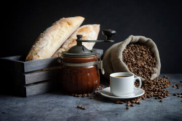 A cup of hot coffee, coffee beans and fresh white bread on a dark background.