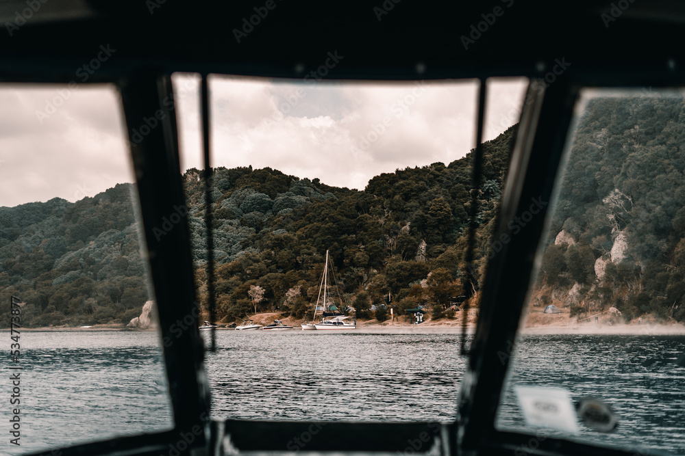 Wall mural view of the catamaran beach and lush forest from inside a boat cruising the lake coming ashore, tara