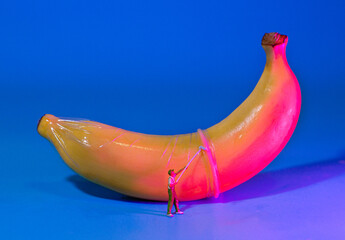 miniature people wear a condom with a banana