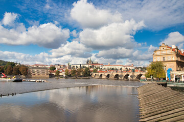 View over Vltava river to Charles bridge, Prague Castle in background under blus sky with white...