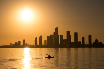A person kayaking in the water at sunset with a city skyline silhouette in the background. Humber Bay, Toronto Ontario