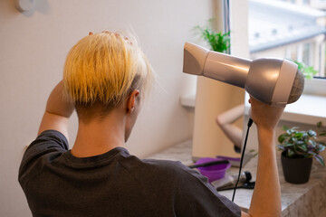 Hair coloring at home. Young man drying his hairs with a hair dryer