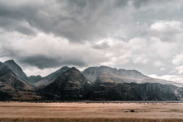 large field on the treeless plain near the lonely sad mountains under a threatening sky with many gray and black clouds on a stormy day, mount cook, new zealand