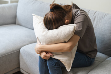Mental health, depressed sad asian young woman, girl sitting on sofa or couch, cover face with pillow. Difficulty, failure and exhausted. Thoughtful worried suffering depression feeling alone at home.
