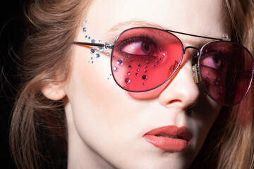 Beauty, fashion and make-up concept. Beautiful girl with pink retro sunglasses and long hair close-up studio portrait. Model with glued jewelers around her eyes looking aside the camera. Retro style