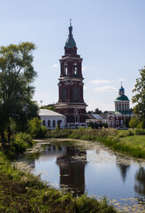 Naklejka premium The ancient bell tower of the Intercession Church with a reflection in the river among green trees on a sunny summer day in Yuriev-Polsky russia