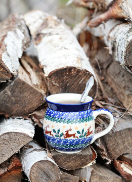 Ceramic mug with tea on the background of birch firewood. Rustic still life. Selective focus