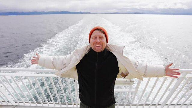 happy man stands with his hands up on the back deck of the ship.