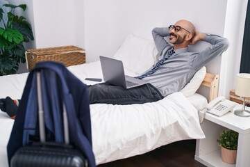 Young hispanic man business worker using laptop relaxed with hands on head at hotel room