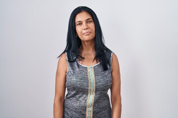 Mature hispanic woman standing over white background relaxed with serious expression on face....