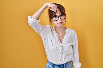 Young beautiful woman wearing casual shirt over yellow background pointing unhappy to pimple on...