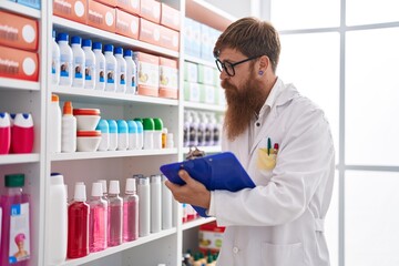 Young redhead man pharmacist writing on document at pharmacy