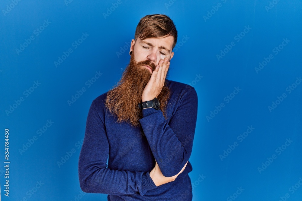 Poster Redhead man with long beard wearing casual blue sweater over blue background thinking looking tired and bored with depression problems with crossed arms.