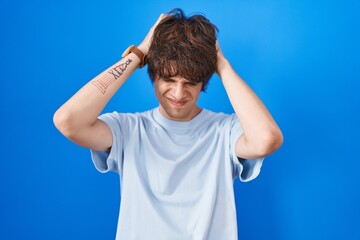 Hispanic young man standing over blue background suffering from headache desperate and stressed because pain and migraine. hands on head.