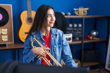 Young hispanic girl musician holding trumpet at music studio