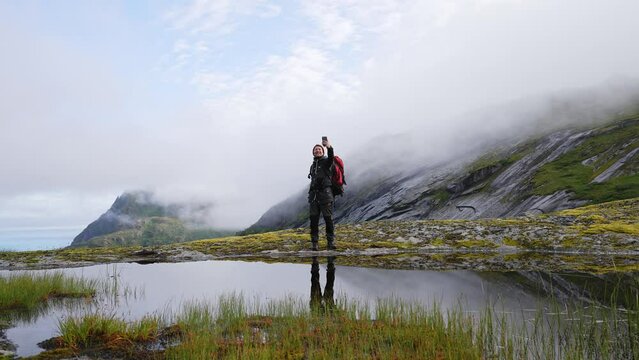 Happy travel blogger taking photo by smartphone hiking with backpack in mountains influencer lifestyle adventure summer tour outdoor in Norway