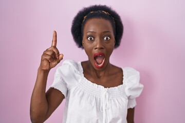 African woman with curly hair standing over pink background pointing finger up with successful idea. exited and happy. number one.