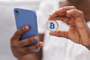 African american woman using smartphone holding bitcoin at home