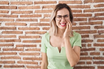 Fototapeta na wymiar Young beautiful woman standing over bricks wall touching mouth with hand with painful expression because of toothache or dental illness on teeth. dentist