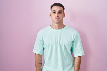 Obraz premium Handsome hispanic man standing over pink background puffing cheeks with funny face. mouth inflated with air, crazy expression.