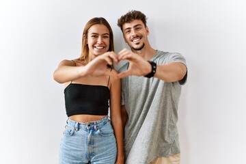 Young beautiful couple standing together over isolated background smiling in love doing heart symbol shape with hands. romantic concept.