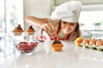 Young beautiful hispanic woman smiling confident putting strawberry on muffin at the kitchen