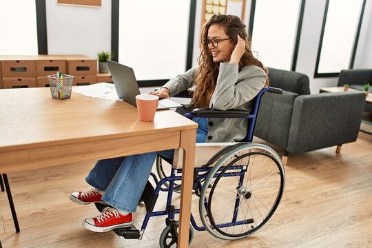 Young beautiful hispanic woman business worker using laptop sitting on wheelchair at office