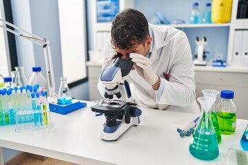 Young hispanic man scientist using microscope at laboratory