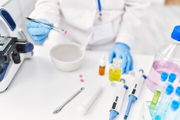 Fototapeta premium Young latin woman wearing scientist uniform holding pill with tweezer at laboratory