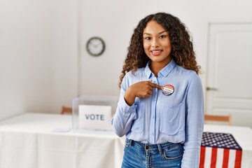 Young latin woman smiling confident pointing with finger to i voted badge at electoral college