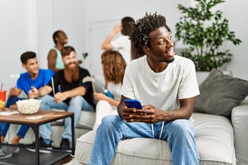 Group of young friends smiling happy sitting on the sofa. Woman using smartphone at home.