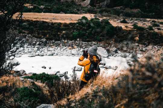 Young Caucasian Woman With A Backpack On Her Back Gray Hat Black Gloves And Orange Jacket Photographing The Beauty Of The Mountains And The Lake In The Middle Of The Calm Nature On A Very Cold Day