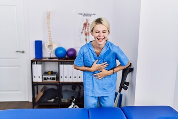 Young physiotherapist woman working at pain recovery clinic smiling and laughing hard out loud because funny crazy joke with hands on body.