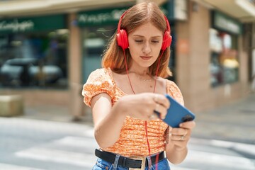 Young redhead woman playing video game at street