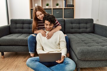 Young couple smiling happy using laptop sitting on the sofa at home.