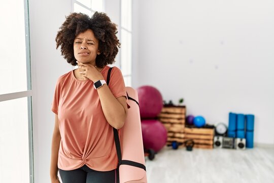 African american woman with afro hair holding yoga mat at pilates room touching painful neck, sore throat for flu, clod and infection
