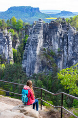 a girl with a backpack sits admiring the view of the massive, unique rock formations in the bohemian switzerland national park in germany  bastei bridge